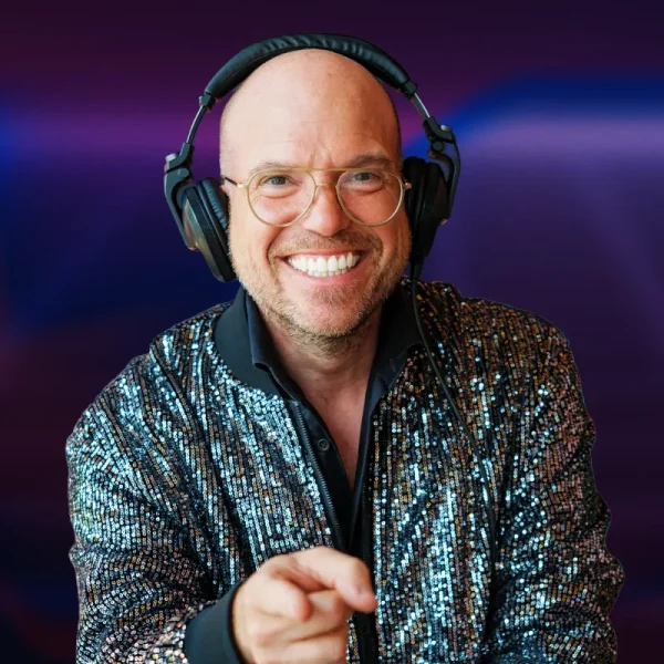 Afbeelding van DJ Royaal (Dimitri Visch) Royaal Artists achter de draaitafels tijdens een bruisend event of cluboptreden. Hij staat gefocust bij zijn apparatuur, omringd door sfeervolle verlichting en een dansend publiek op de achtergrond