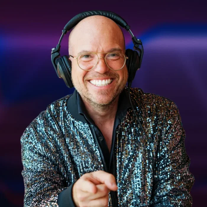 Afbeelding van DJ Royaal (Dimitri Visch) Royaal Artists achter de draaitafels tijdens een bruisend event of cluboptreden. Hij staat gefocust bij zijn apparatuur, omringd door sfeervolle verlichting en een dansend publiek op de achtergrond